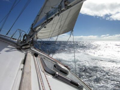 Ein weißes Segelboot steuert auf offenem Meer der Sonne entgegen