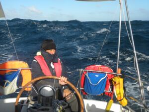 Eine warm gekleidete Person mit roter Rettungsweste steuert ein Boot durch hohen Seegang