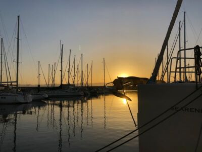 Eine im Hafen untergehende Sonne spiegelt sich in der glatten Wasseroberfläche